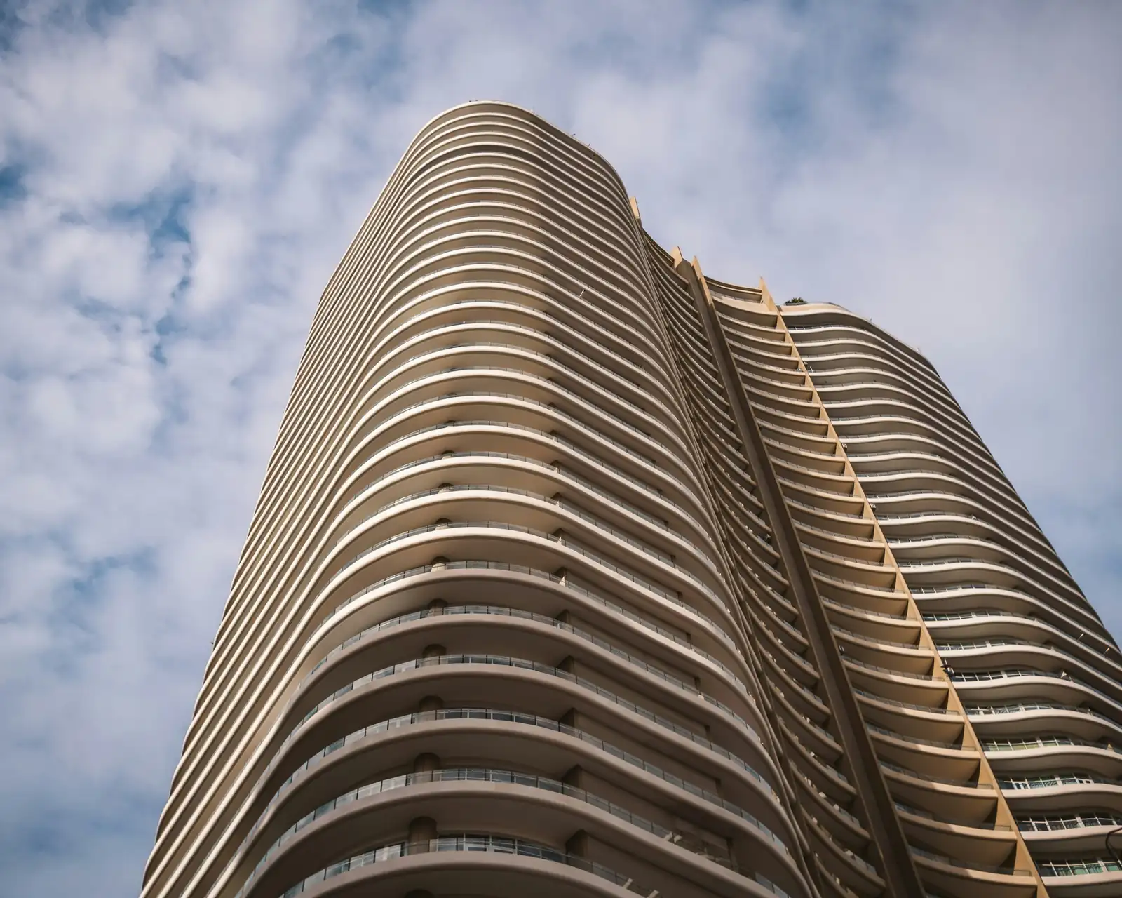 Upward view of a curved high-rise condo tower with rounded balconies against a blue sky