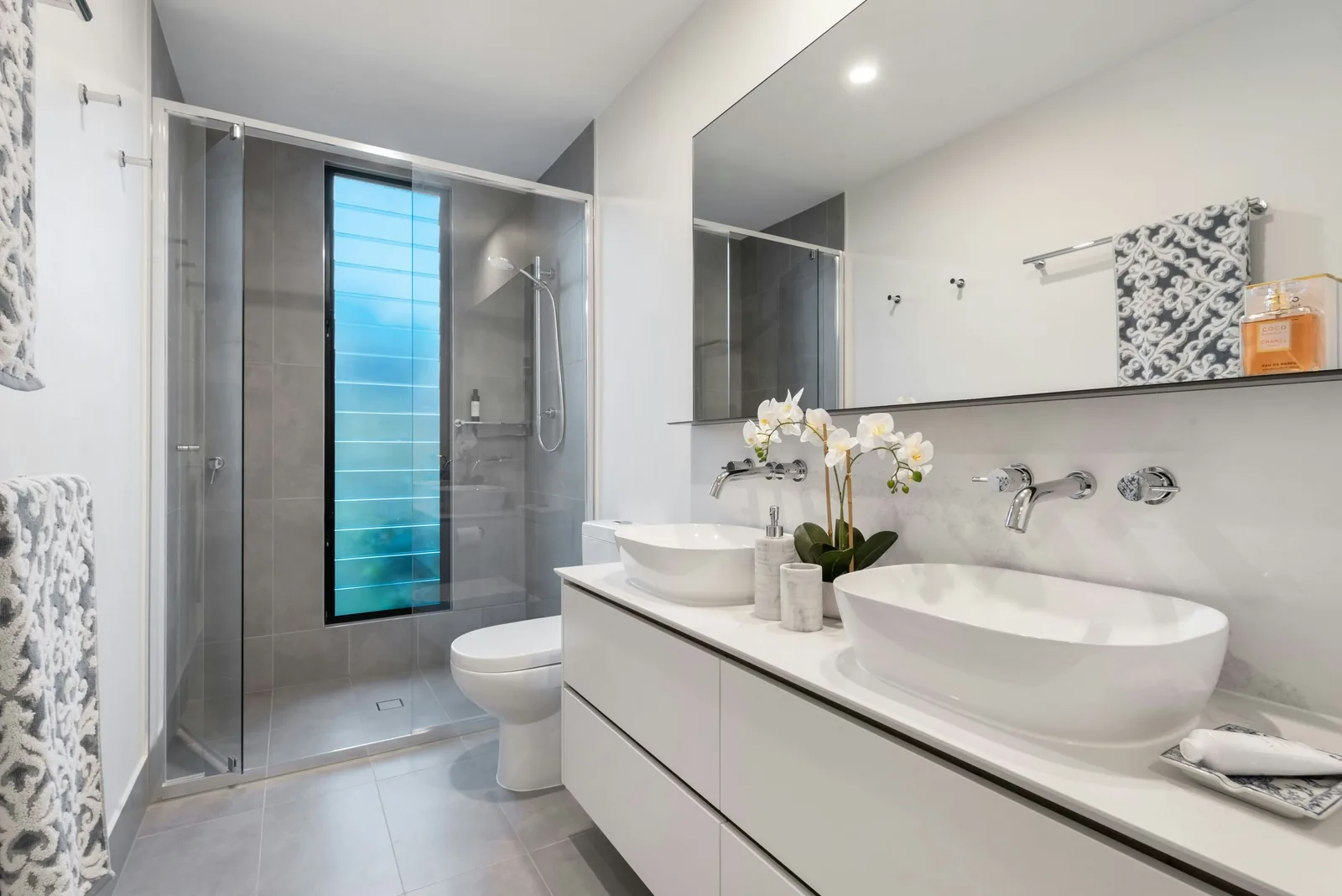 Sleek modern bathroom with a white double vanity, oval vessel sinks, and a glass-enclosed shower