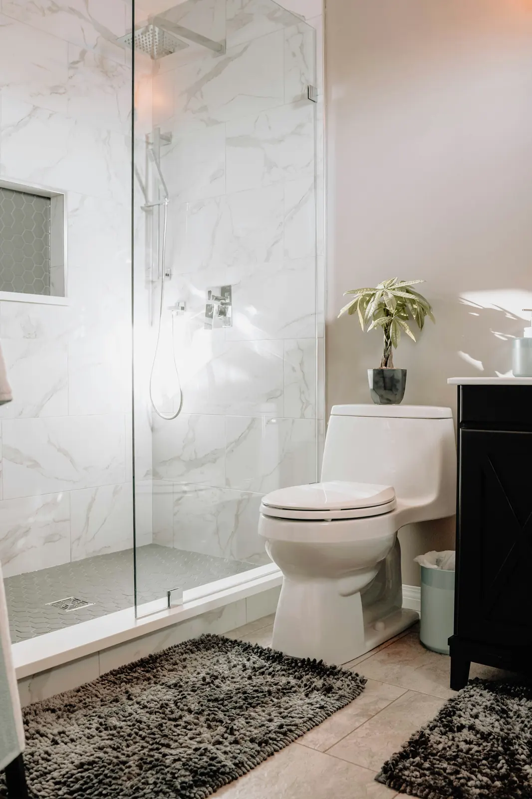 Frameless glass shower enclosure with marble tile walls and sunlit natural light