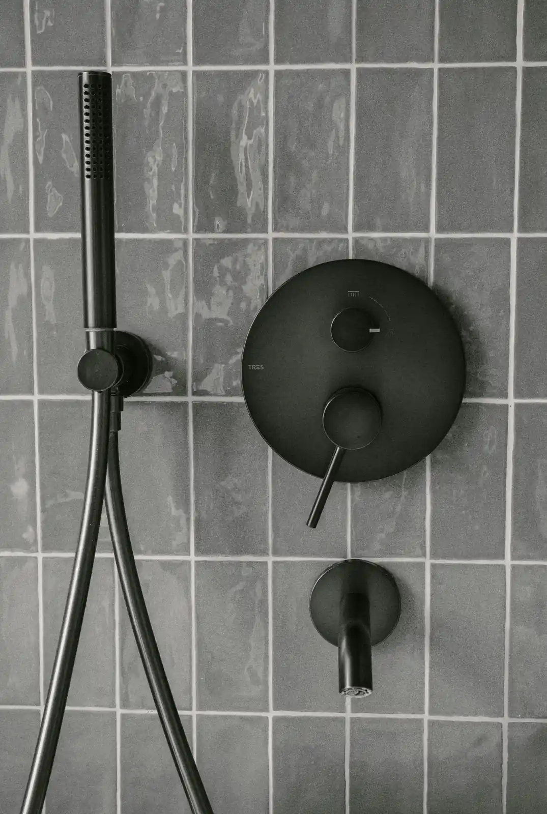 Modern matte black shower fixtures and hand shower mounted on grey tile