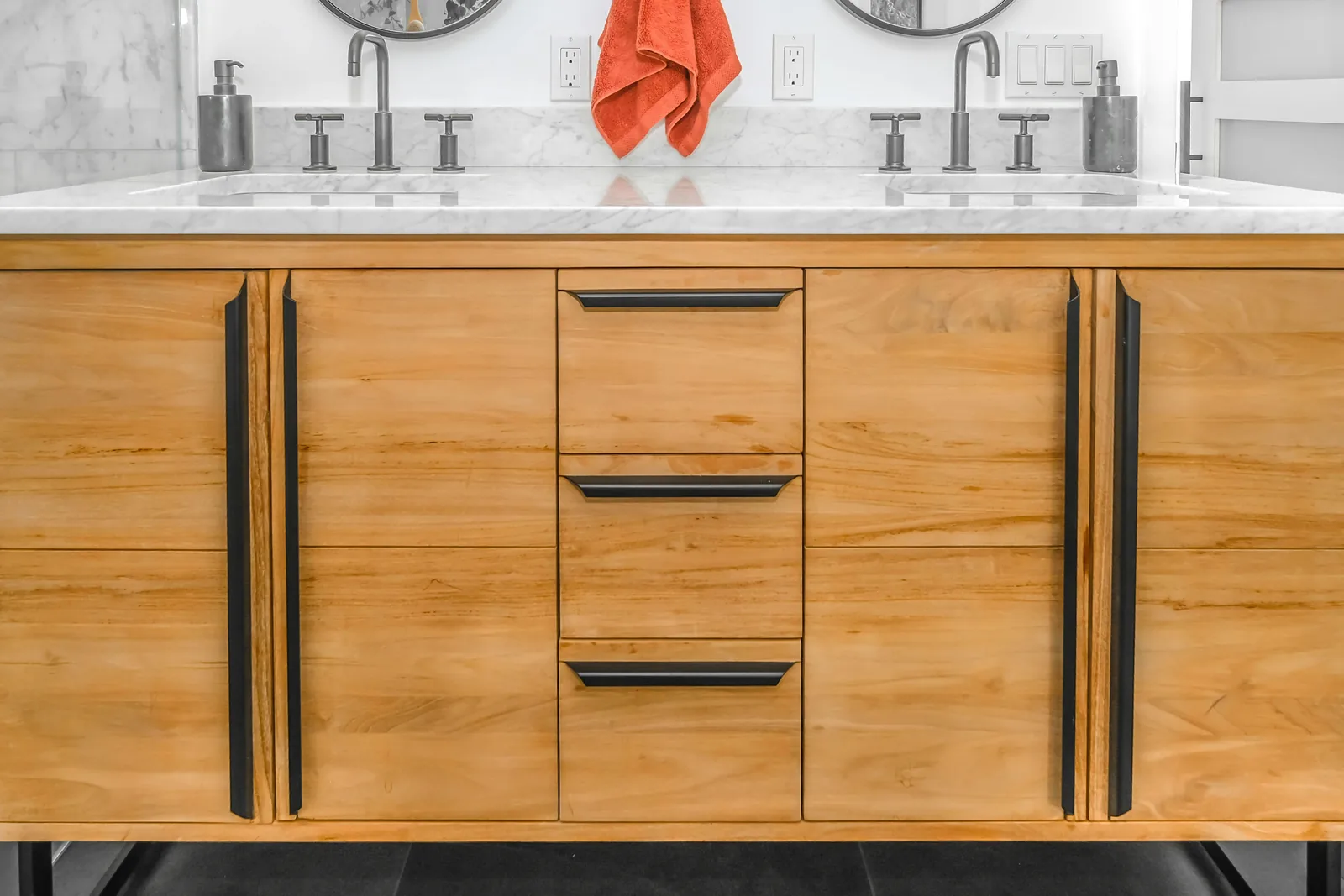Warm wood double-vanity cabinetry with black drawer pulls beneath a white marble countertop