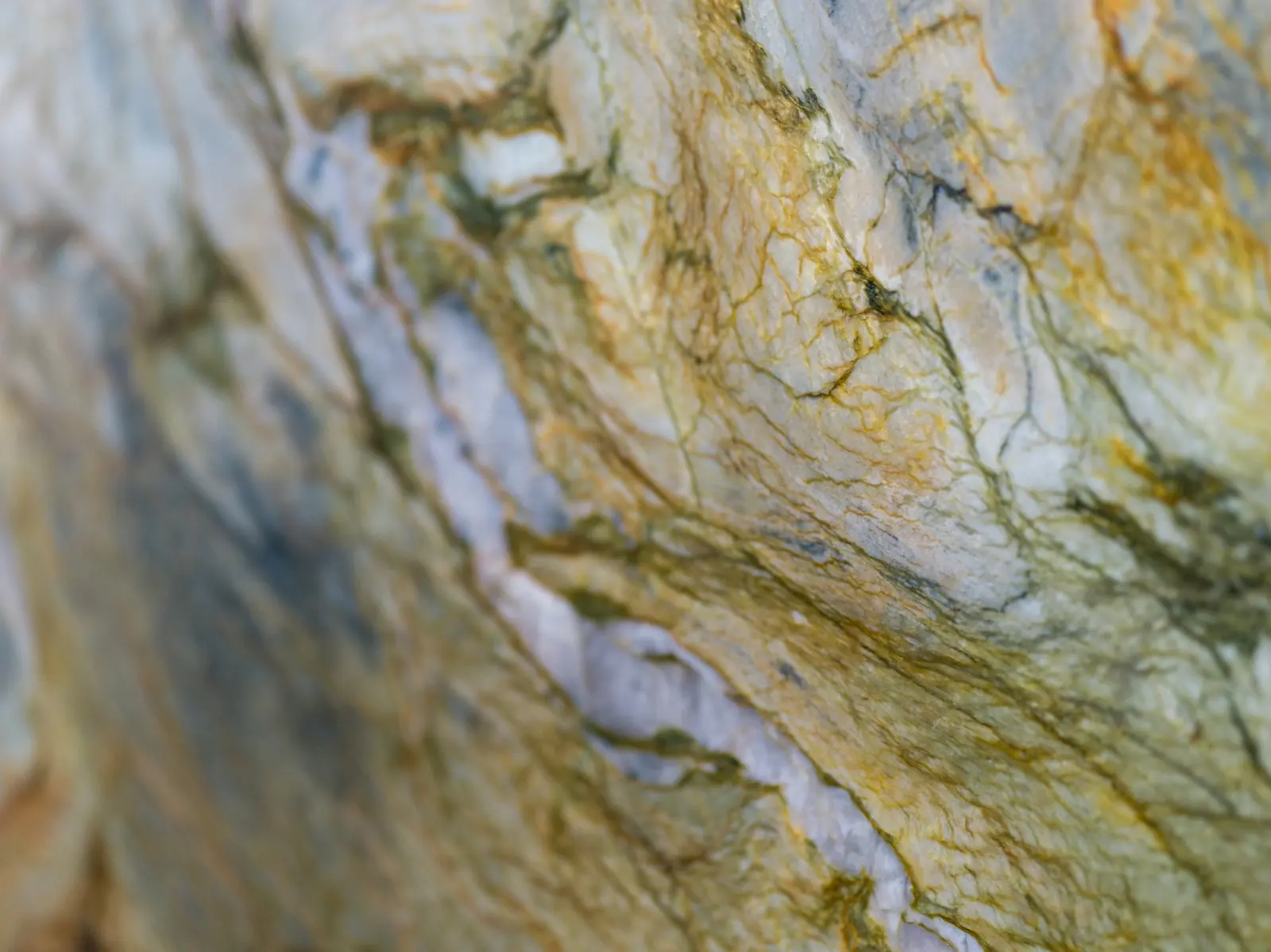 Close-up of natural stone slab with gold and green veining running through pale marble
